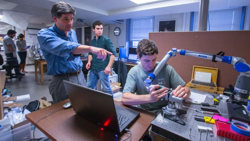 Senior scientist John Wilson directs student Brady Anthony-Brumfield in measuring a part milled in the astronomy machine shop.