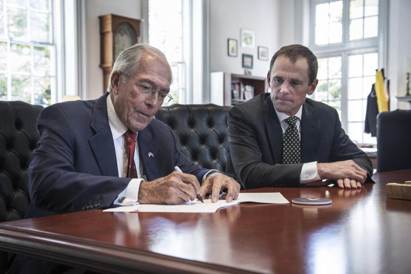 John Nau signs a document with President Jim Ryan